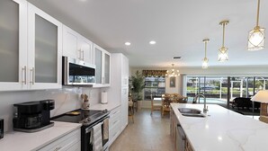A modern kitchen with white cabinets, a large island with a sink, and a view of a pool and outdoor seating area.