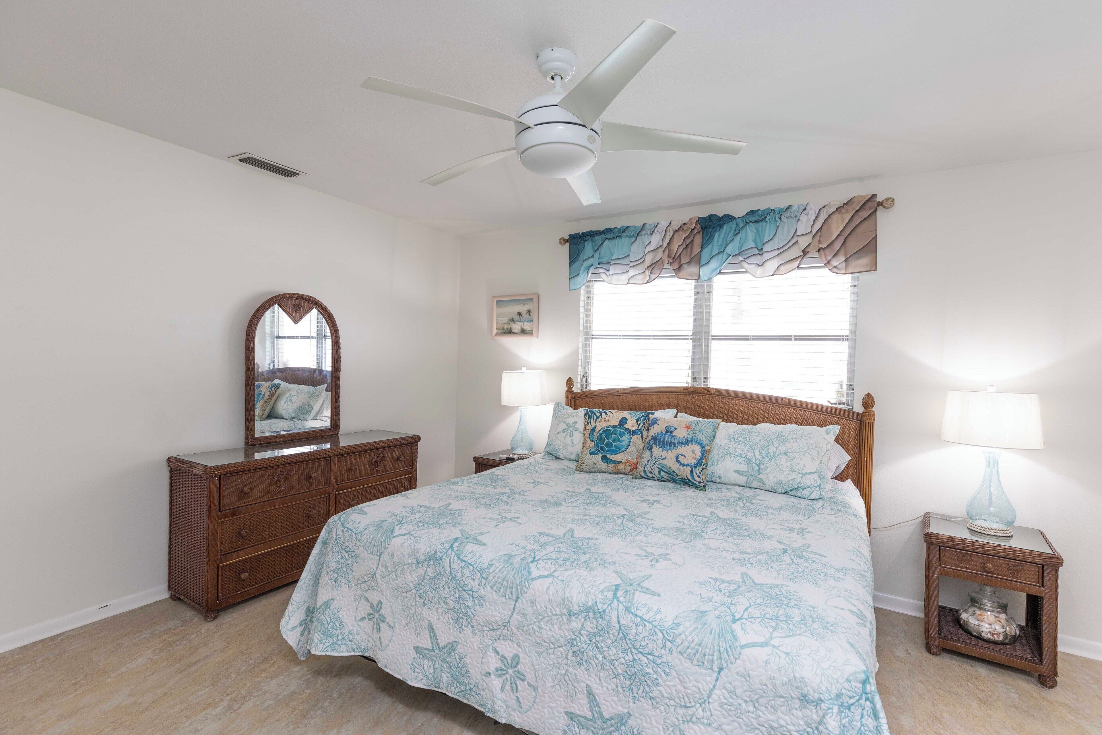 A bedroom with a bed, a dresser, a mirror, a nightstand, a lamp, and a ceiling fan.