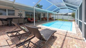A covered outdoor pool area with lounge chairs, a barbecue setup, and a view of the pool.
