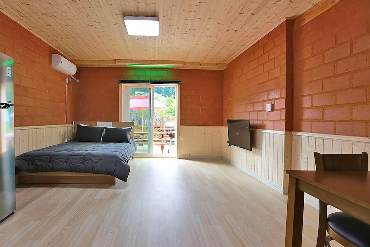 A room with a bed, a refrigerator, a wooden ceiling, and a view of the outside.