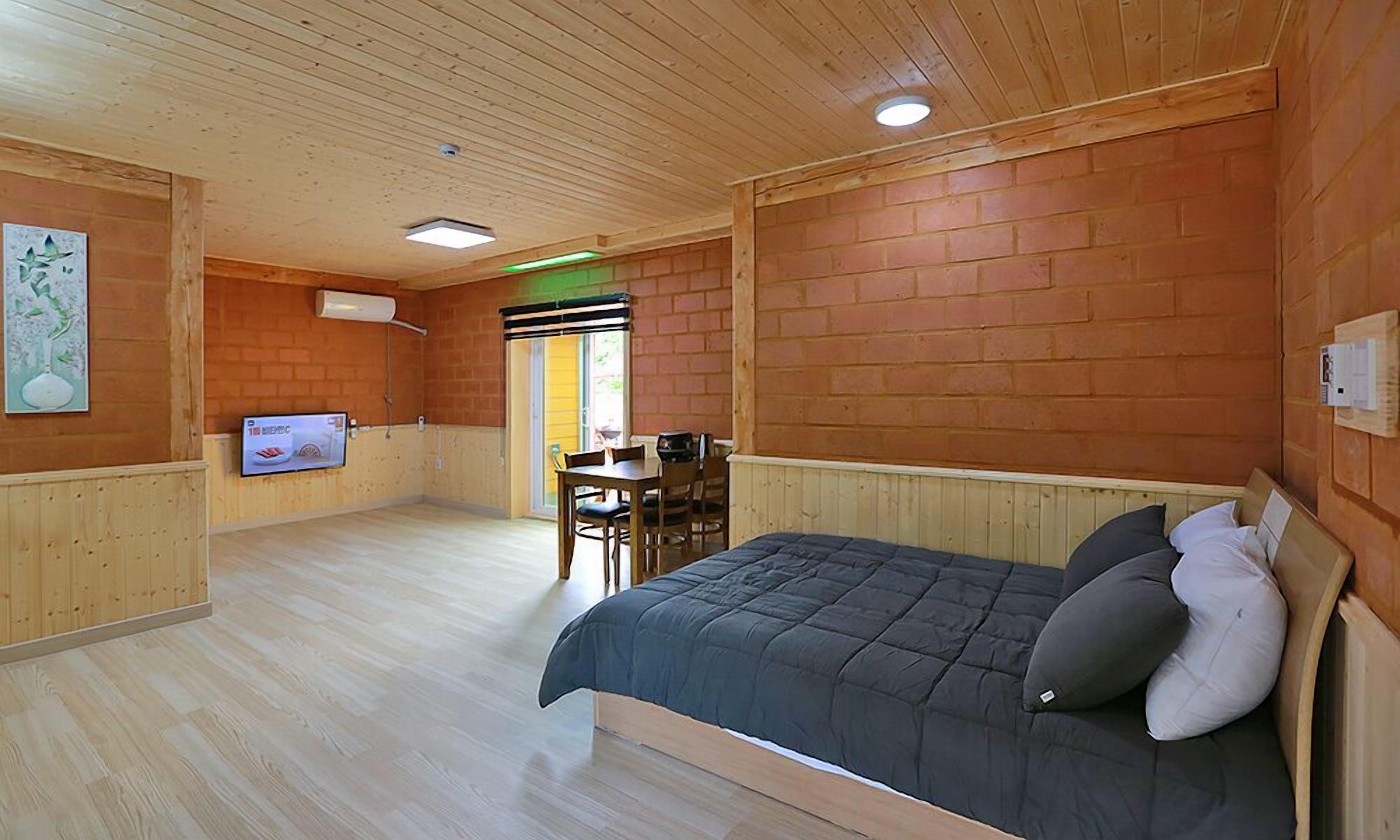A wooden-paneled room with a bed, a television, and a dining area.