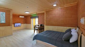 A wooden-paneled room with a bed, a television, and a dining area.