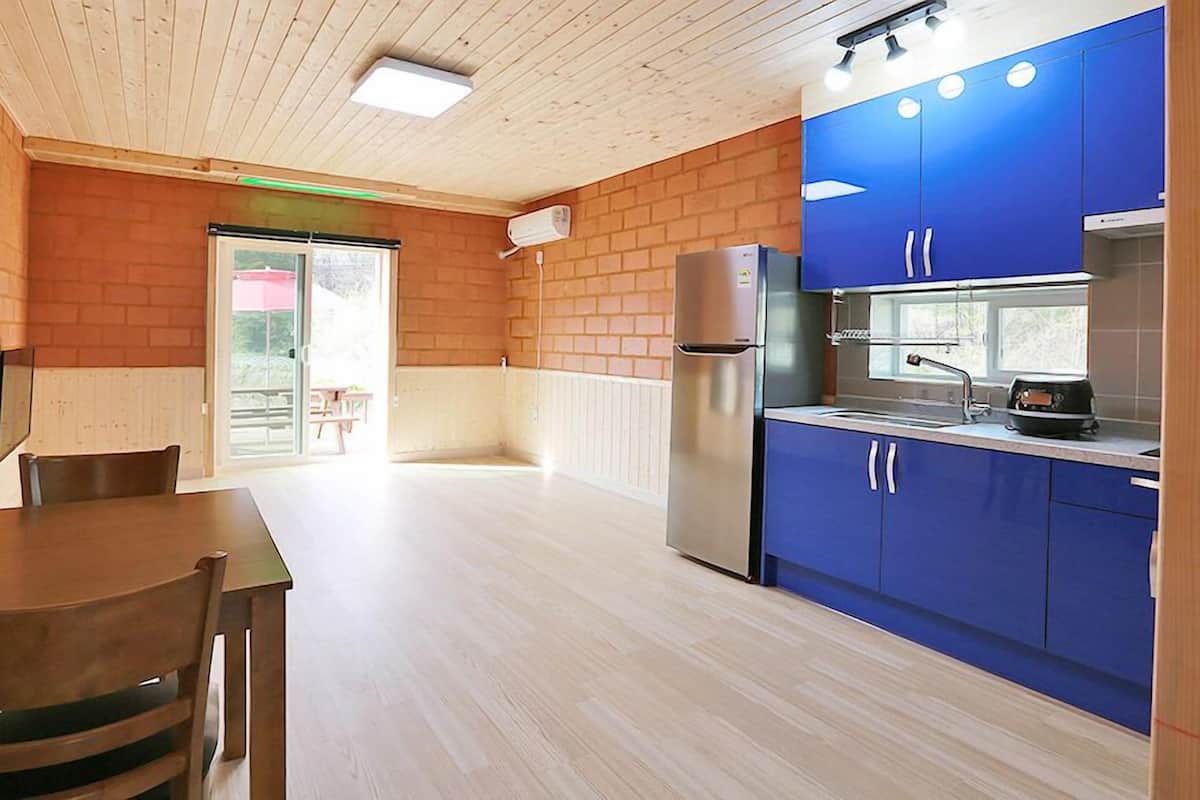 A modern kitchen with blue cabinets, a stainless steel refrigerator, and a wooden dining table with chairs.