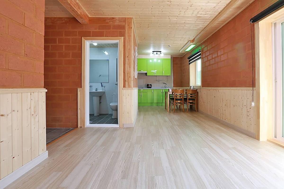 A spacious room with wooden flooring, a kitchen area with green cabinets, and a visible bathroom.