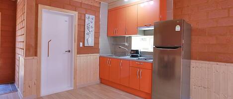 A compact kitchen with wooden cabinets, a stainless steel refrigerator, and a white door.