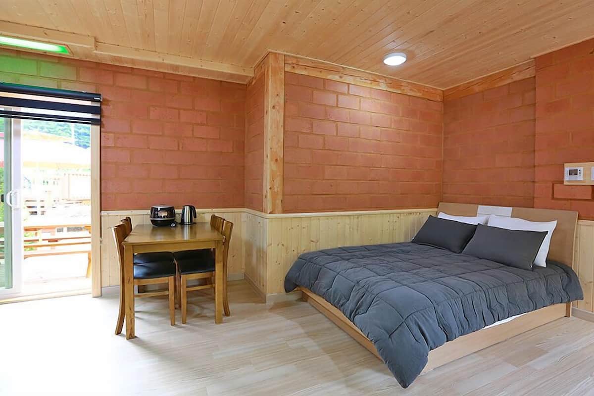 A room with a bed, a table with chairs, and a brick wall.