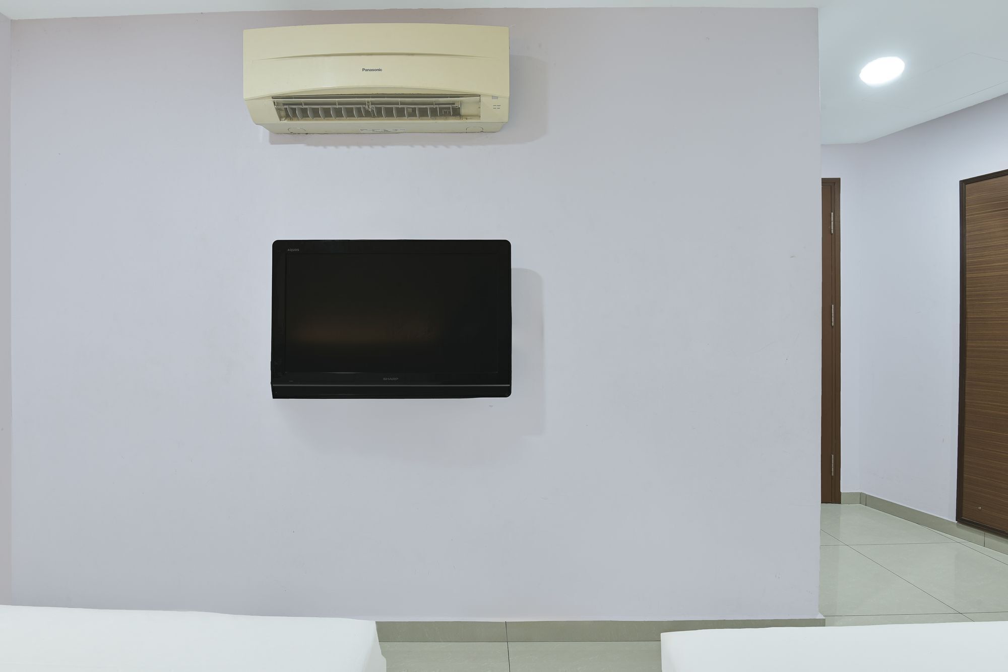 A room with a mounted air conditioner, a flat-screen TV, and a wooden door.