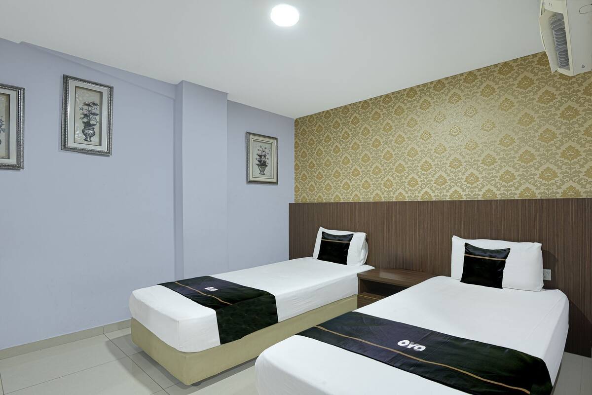 A hotel room with two single beds, a small table, and a wall-mounted air conditioner.
