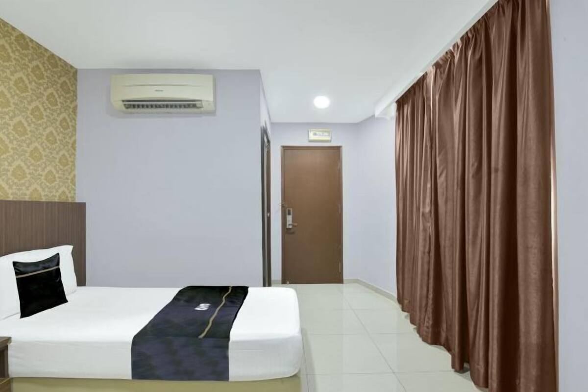 A hotel room with a bed, an air conditioning unit, a door, and a curtain.