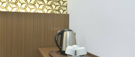 A coffee maker on a tray with a white mug holder, a kettle, and a wooden panel with a geometric pattern.