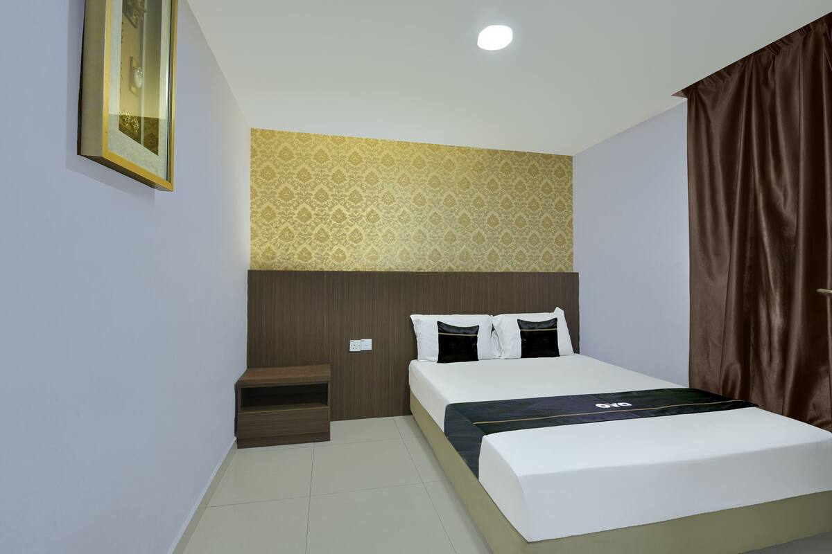A hotel room with a bed, a small seating area, a patterned wall, and a window with curtains.