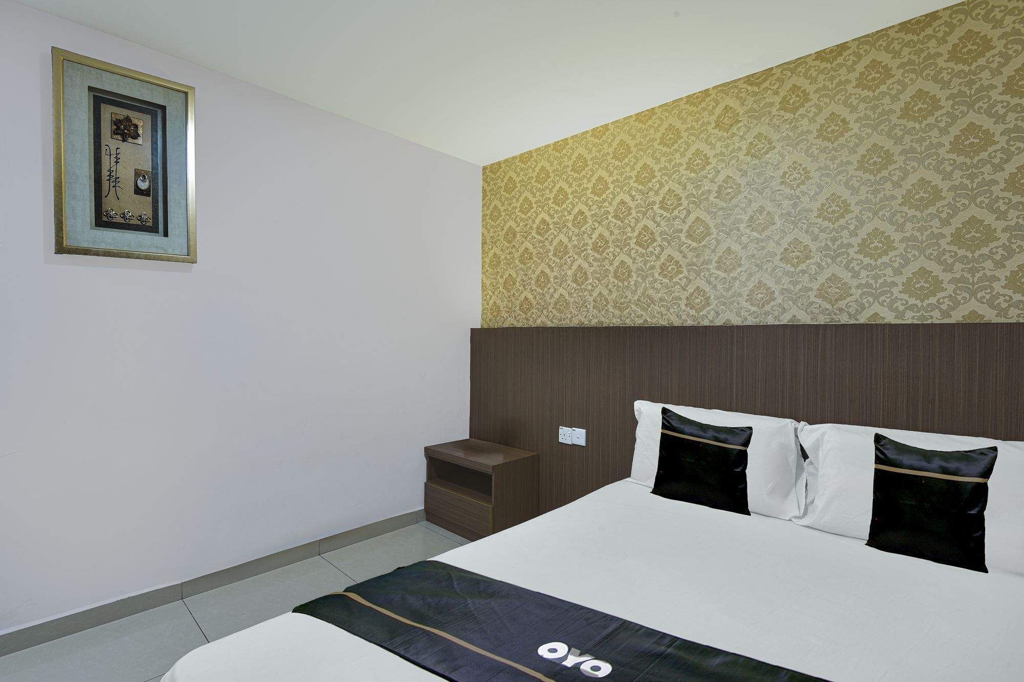 A hotel room with a bed, a nightstand, a wall-mounted picture, and a patterned wallpaper.
