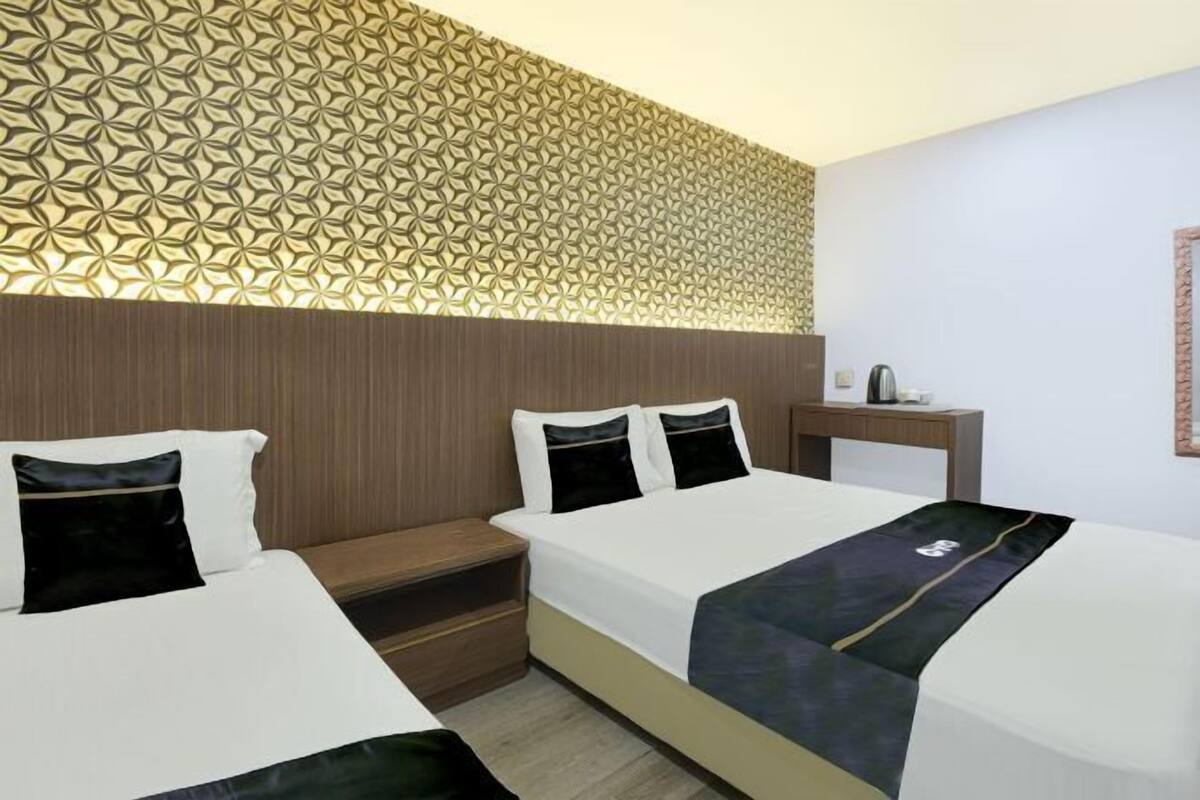 A hotel room with two beds, a nightstand, a wall with a geometric pattern, and a small table with a kettle.