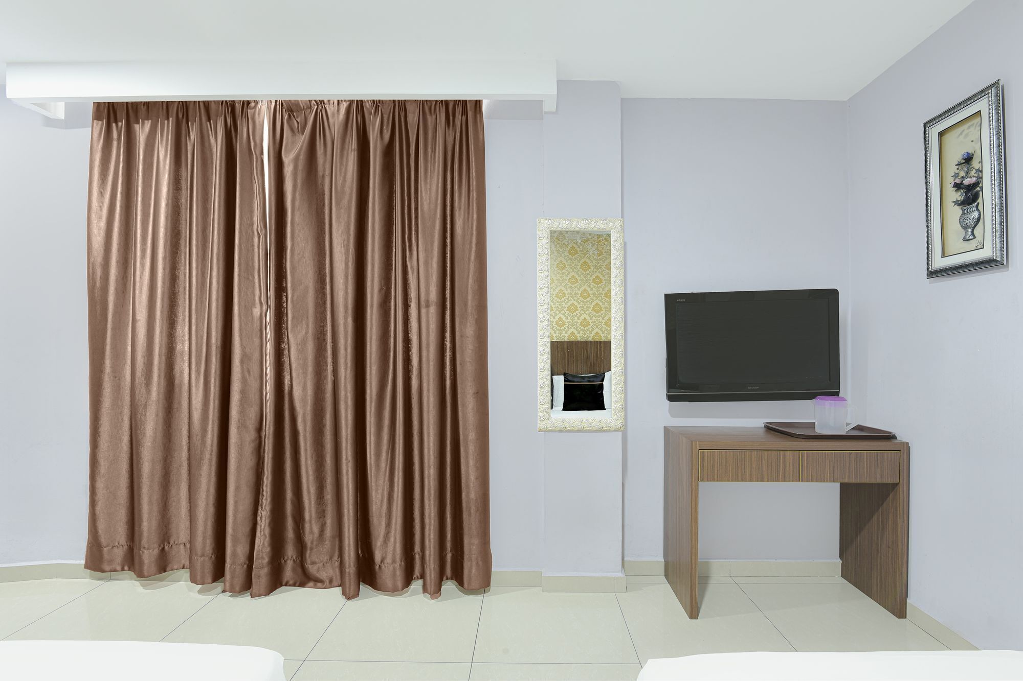 Una habitación con un ventanal cubierto por cortinas marrones, un televisor de pantalla plana sobre un soporte de madera y un cuadro enmarcado en la pared.