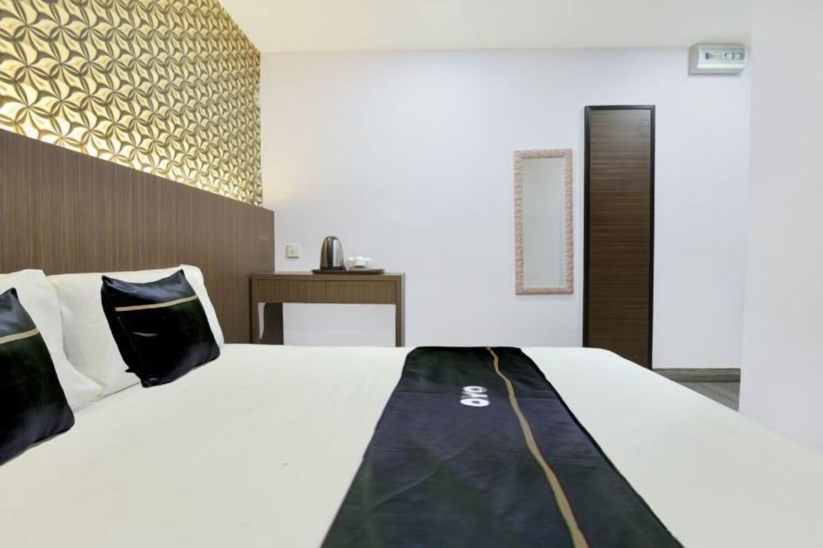 A hotel room with a bed, a bedside table with a lamp, a mirror, and a door.