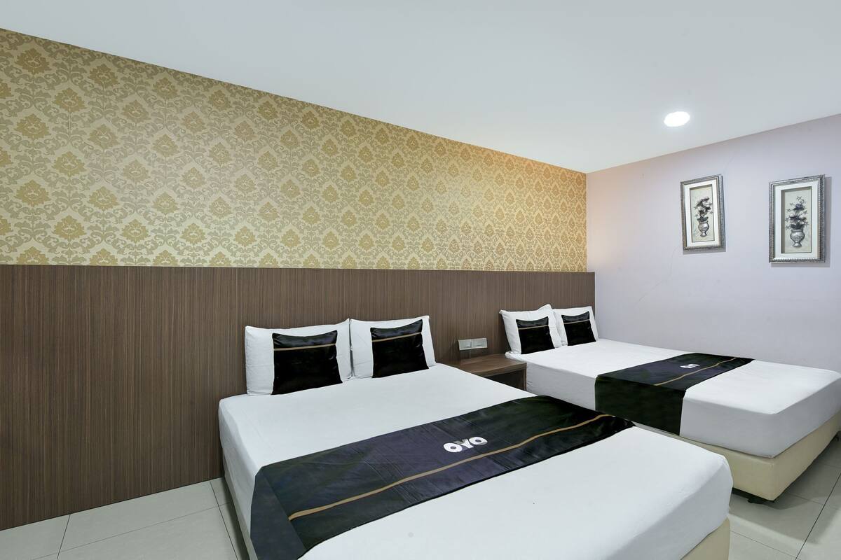 A hotel room with two beds, a patterned wallpaper, and framed artwork on the wall.