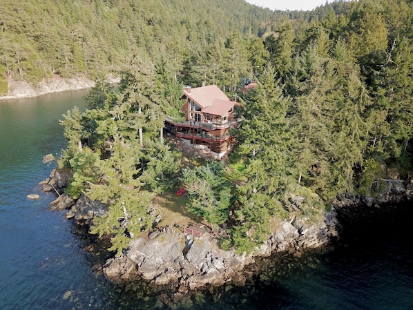 A cabin on a rocky island surrounded by dense forest and a lake.
