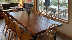 Un comedor de madera con una mesa grande y sillas, una araña y ventanas amplias que ofrecen vistas al exterior.
