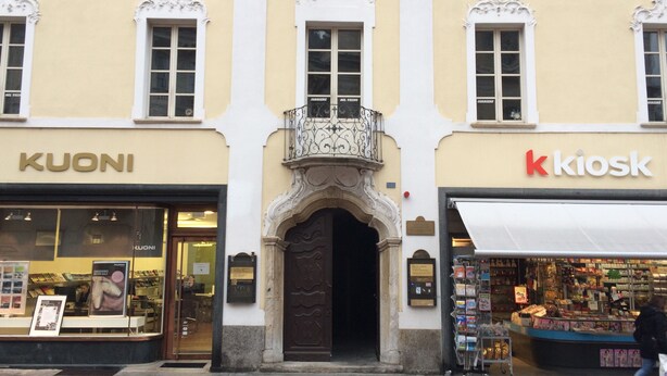 A building facade with storefronts labeled 'KUONI' and 'kiosk'. - Piazza Collegiata Bellinzona (Bellinzona)