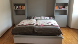 A bedroom with a bed, two bookshelves, and a wooden floor. - Piazza Collegiata Bellinzona (Bellinzona)