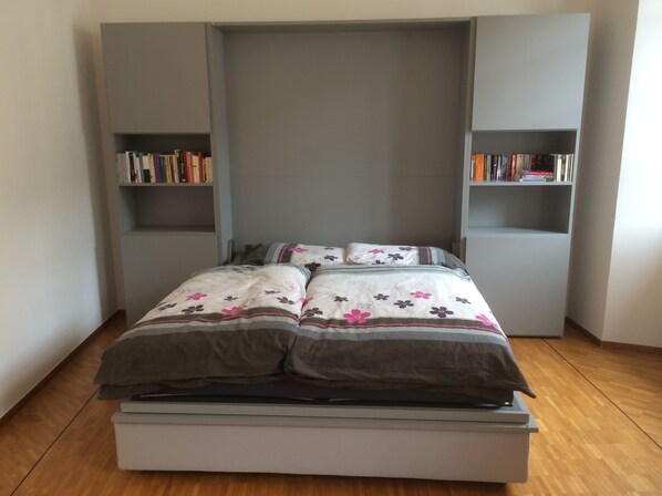 A bedroom with a bed, two bookshelves, and a wooden floor.