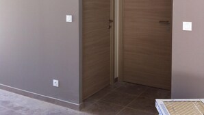 Een kamer met een houten deur, een witte airconditioning die aan de muur is bevestigd, en een betegelde vloer.