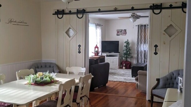 Un área de comedor con una mesa y sillas blancas, un ventilador de techo y vista al salón.