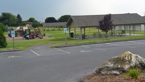 Un parque infantil con tobogán, columpios, mesas de picnic y un pabellón cubierto.