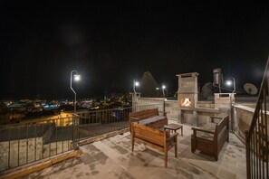 A rooftop terrace with a stone bench, a small table, and a fire feature. - Charming Cave Hotel (Nevsehir)