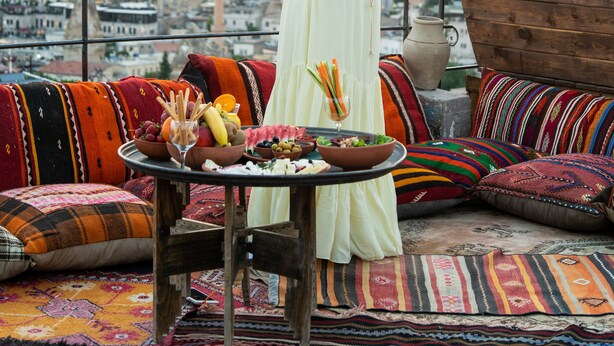 A woman in a white dress on a balcony overlooking a city with colorful textiles and a table with food and drinks. - Charming Cave Hotel (Nevsehir)