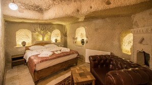 A cozy bedroom with a wooden bed, a leather sofa, and stone walls. - Charming Cave Hotel (Nevsehir)