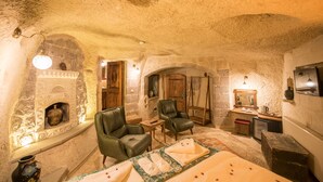 A stone-walled room with a fireplace, two leather chairs, a small table, and a mirror. - Charming Cave Hotel (Nevsehir)