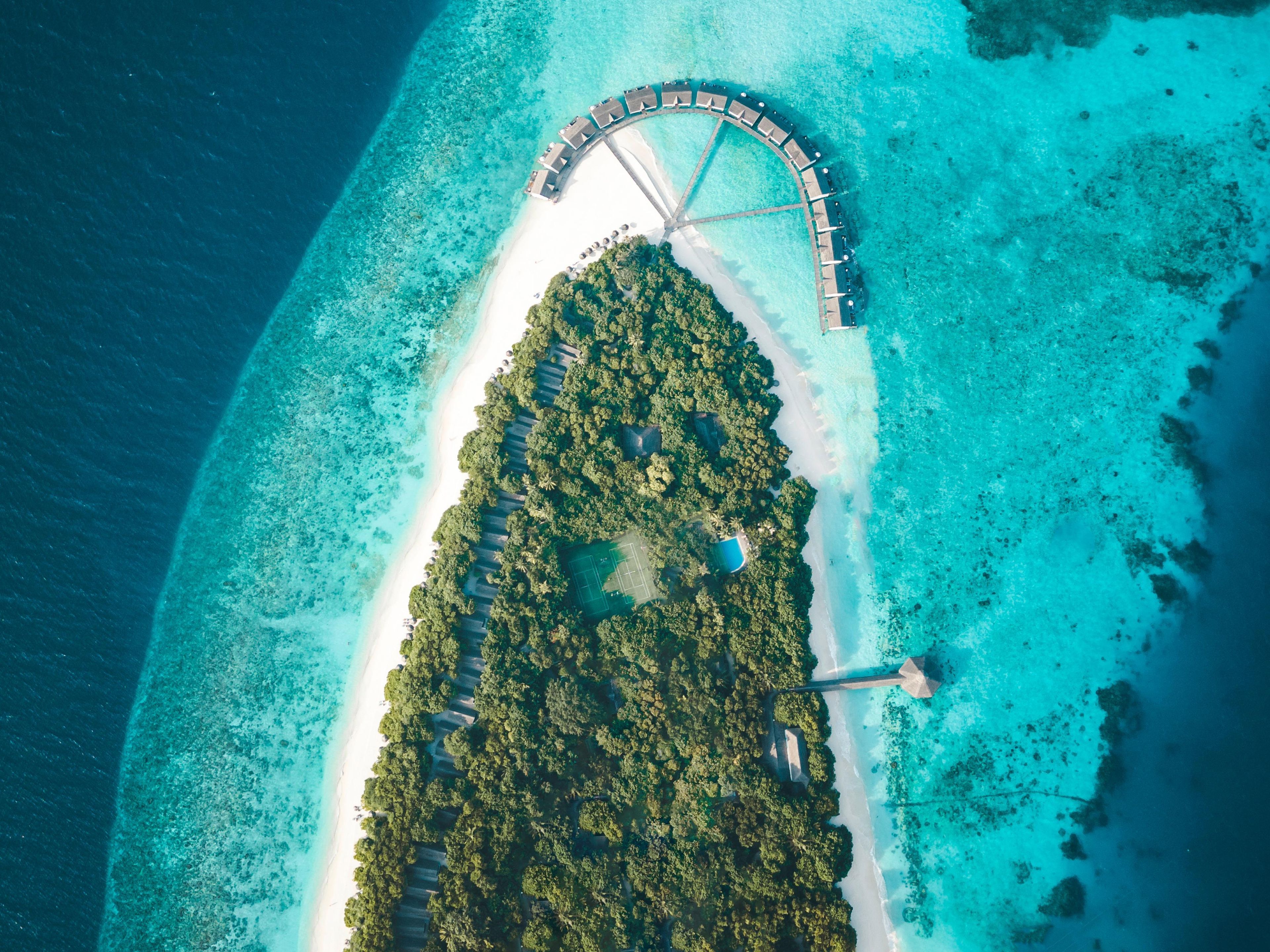 Vista aérea de uma ilha tropical com uma área de resort circular, uma praia e uma área arborizada.