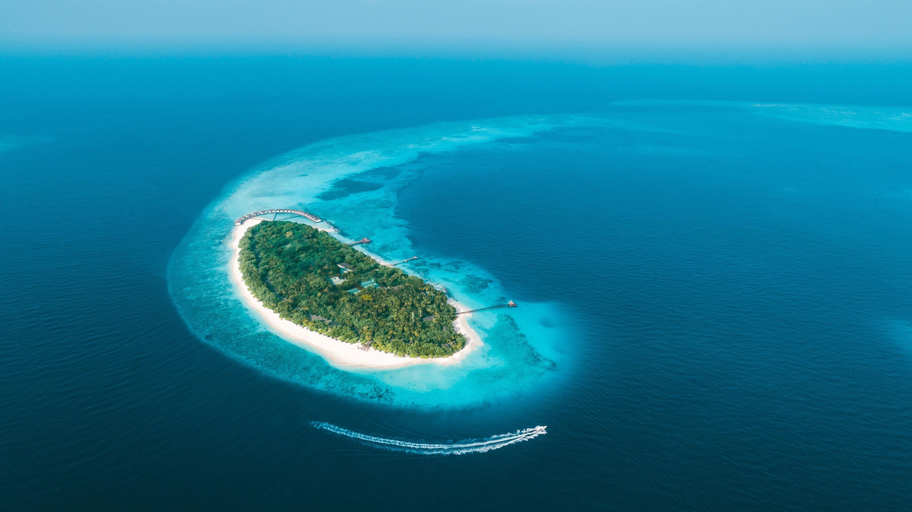 An aerial view of a tropical island with a curved shoreline, surrounded by clear blue waters.