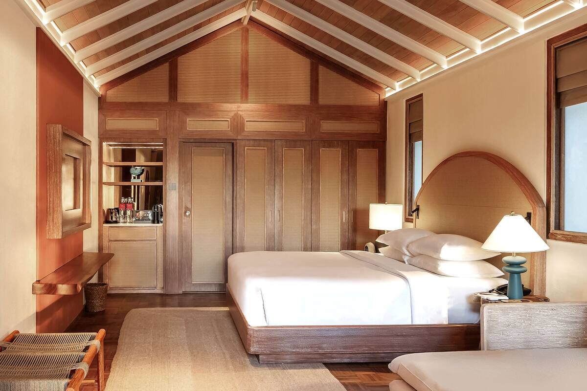 A bedroom with a large bed, a nightstand, a lamp, and a wooden wardrobe.