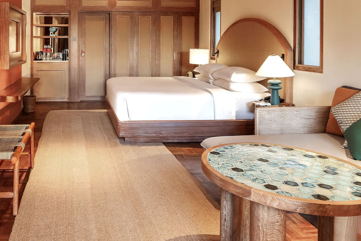 A hotel room with a bed, bedside table, lamp, and a small round table with a mosaic top.