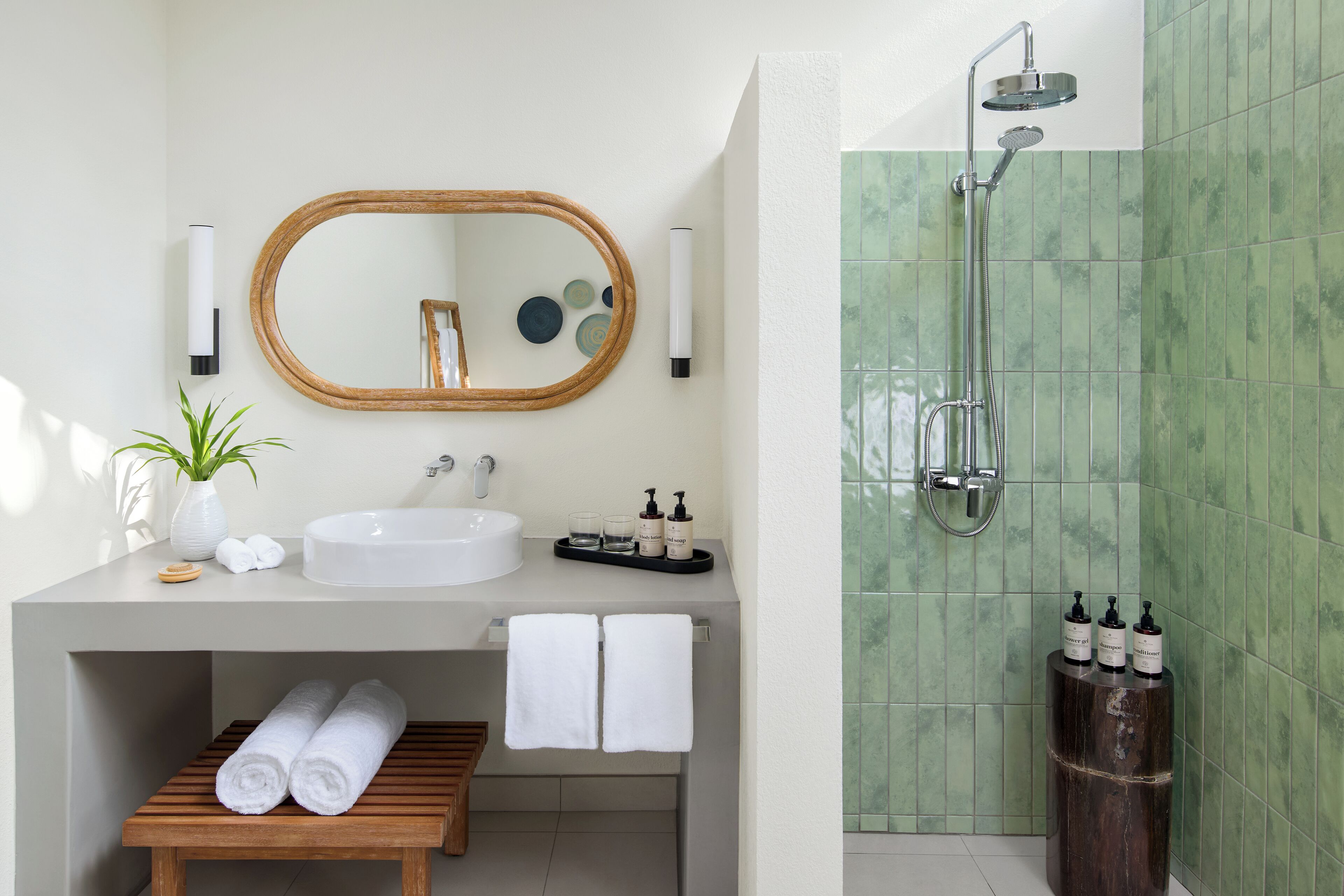 Un baño moderno con un espejo grande, un lavabo blanco y una ducha con azulejos verdes.