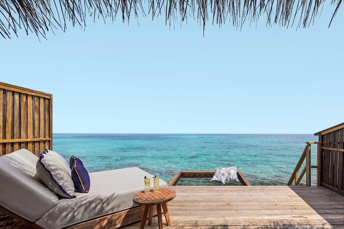 A wooden deck with a sofa and a small round table, overlooking a clear blue sea.