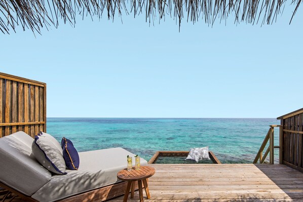 A wooden deck with a sofa and a small round table, overlooking a clear blue sea. - NH Collection Maldives Reethi Resort (Fonimagoodhoo)