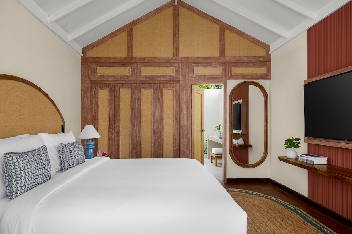 Una habitación de hotel con una cama grande, televisión, espejo y puerta de madera.