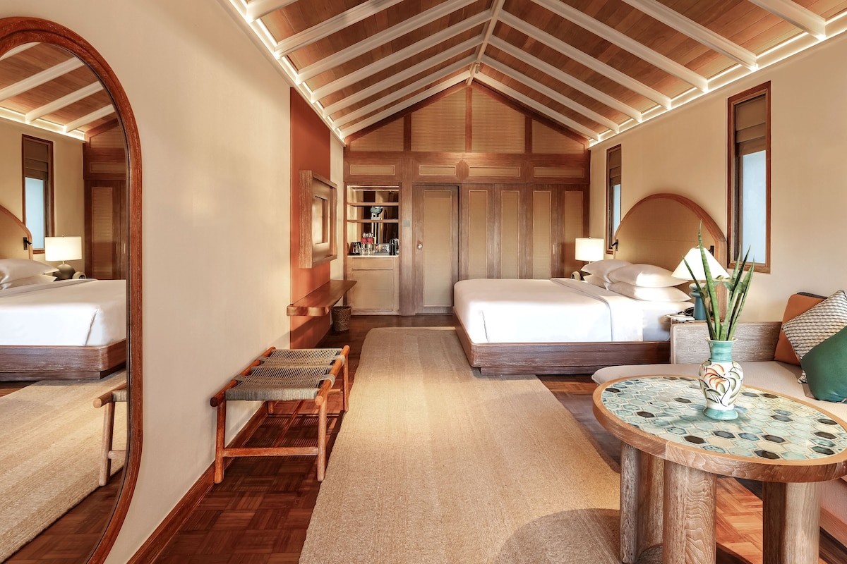 Un dormitorio amplio con una cama grande, otra cama más pequeña, un área de descanso con una mesa y un espejo.
