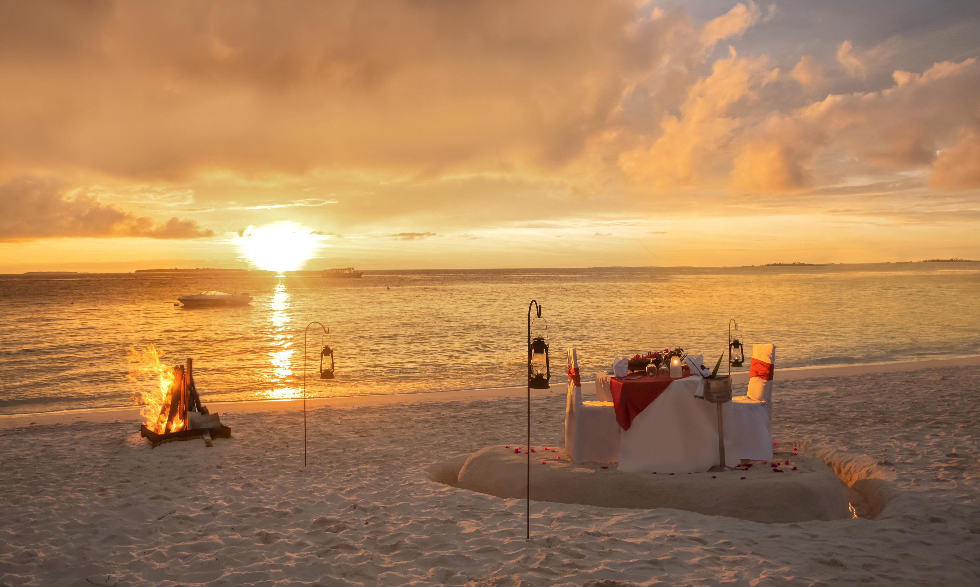 A beach scene with a sandcastle, a fire, and a table with a lantern.