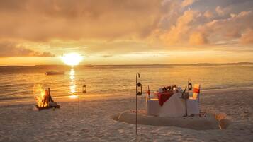 A beach scene with a sandcastle, a fire, and a table with a lantern.