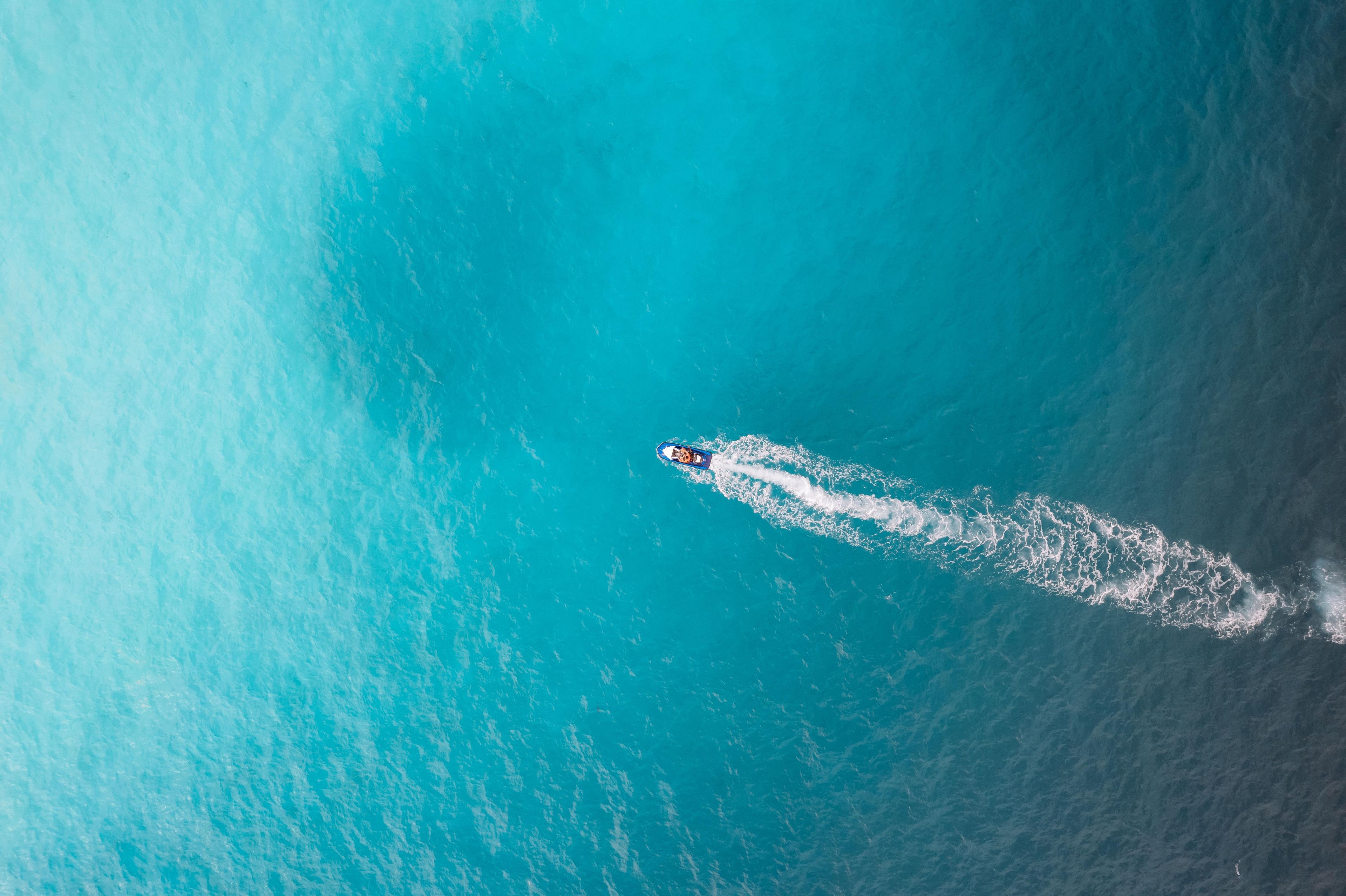 An aerial view of a boat creating a wake in turquoise water.