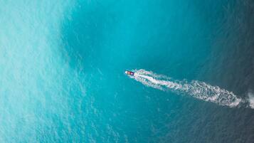 An aerial view of a boat creating a wake in turquoise water.