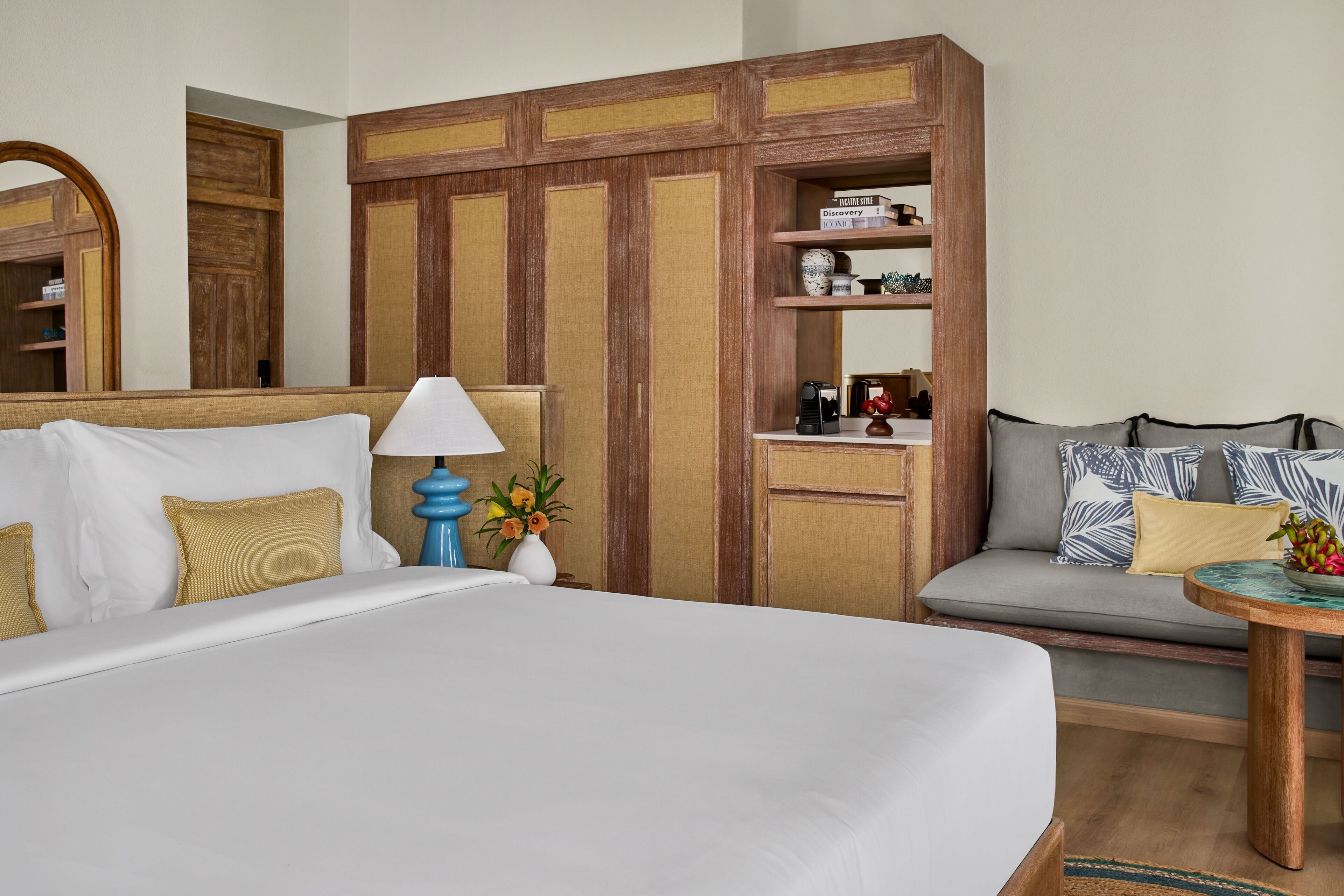 Une chambre d’hôtel avec un grand lit, un canapé, une petite table, une machine à café et une étagère avec des livres et des objets décoratifs.