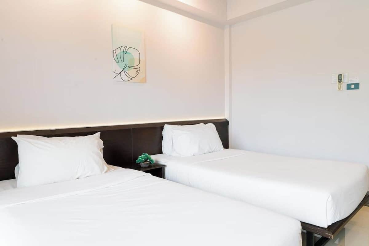 A hotel room with two single beds, a nightstand with a green plant, and a wall-mounted light fixture.