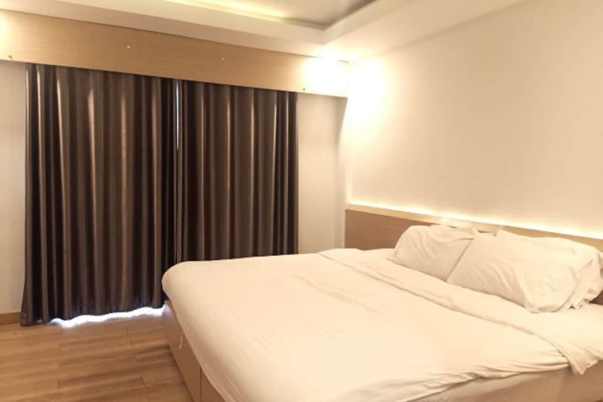 Una habitación de hotel con cama, cortinas y una lámpara fijada a la pared.