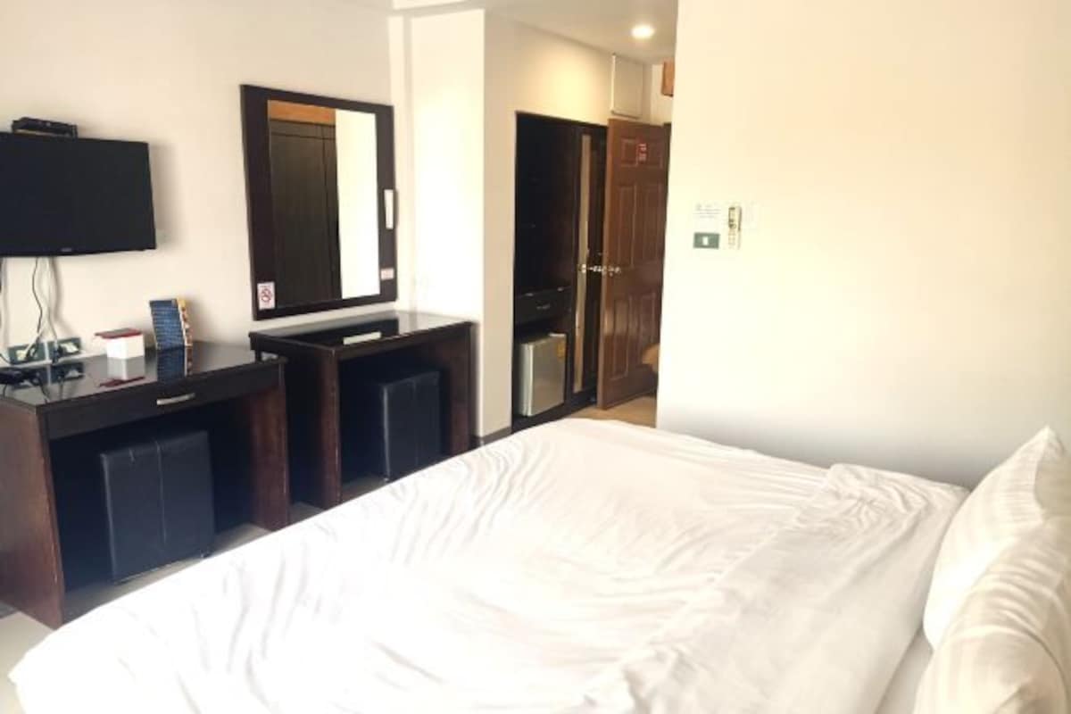 Una habitación de hotel con cama, escritorio, ordenador, televisor y espejo.