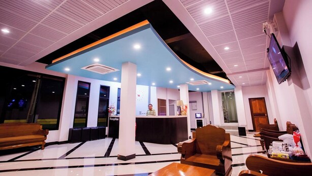 A hotel reception area with a reception desk, seating area, and a TV mounted on the wall. - Smile Place Hotel Chiang Rai (Chiang Rai)